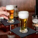 Two Libbey Pilsner glasses of beer with foam on a bar counter.