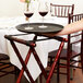 A person using a Tablecraft mahogany wood tray stand to hold a tray with two glasses of wine.