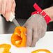 A person cutting a bell pepper with a knife while wearing a Victorinox red cut resistant glove.