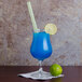 A blue drink in an Arcoroc Petite Cuvee glass with a straw and lime wedge.
