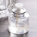 A close-up of a Sterno clear liquid candle fuel cartridge in a glass bottle with a lid.