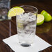 A highball glass of water with ice and lime wedges on a table.