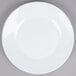 An Arcoroc white glass lunch plate with a white rim on a gray surface.