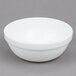 An Arcoroc white stacking bowl on a gray surface.