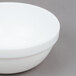 An Arcoroc white stacking bowl with a white rim on a gray surface.