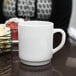 A close-up of a white Arcoroc stacking mug on a table.