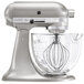 A KitchenAid premium metallic silver stand mixer with a glass bowl.