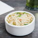 A Tuxton white china bowl filled with noodle soup topped with a green leaf.