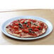 A Tuxton porcelain white china pizza plate with a pizza topped with tomatoes and olives.