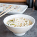 A Tuxton white mini round china bowl filled with noodle soup with chopsticks in it.