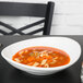 A Tuxton white oval china bowl filled with soup, noodles, and vegetables on a table.