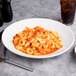 A Tuxton porcelain white pasta bowl filled with pasta and a glass of a drink on the side.