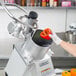 A person using a Hobart food processor to push a red bell pepper through a disc.