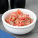 A Tuxton white china bowl filled with salsa on a table.