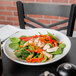 A Tuxton white china pasta bowl filled with salad with chicken and vegetables on a table.
