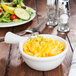 A Tuxton French casserole dish filled with macaroni and cheese on a table next to a salad.