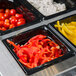 A Vollrath black polycarbonate food pan containing a tray of food with different colored peppers.