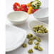 A white Tuxton oval china bowl filled with green tortellini and peppers.
