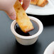A person dipping a piece of croissant into a Tuxton eggshell ramekin of sauce.