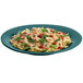 A Tablecraft hunter green cast aluminum platter with a wide rim holding a plate of pasta with shrimp and vegetables.