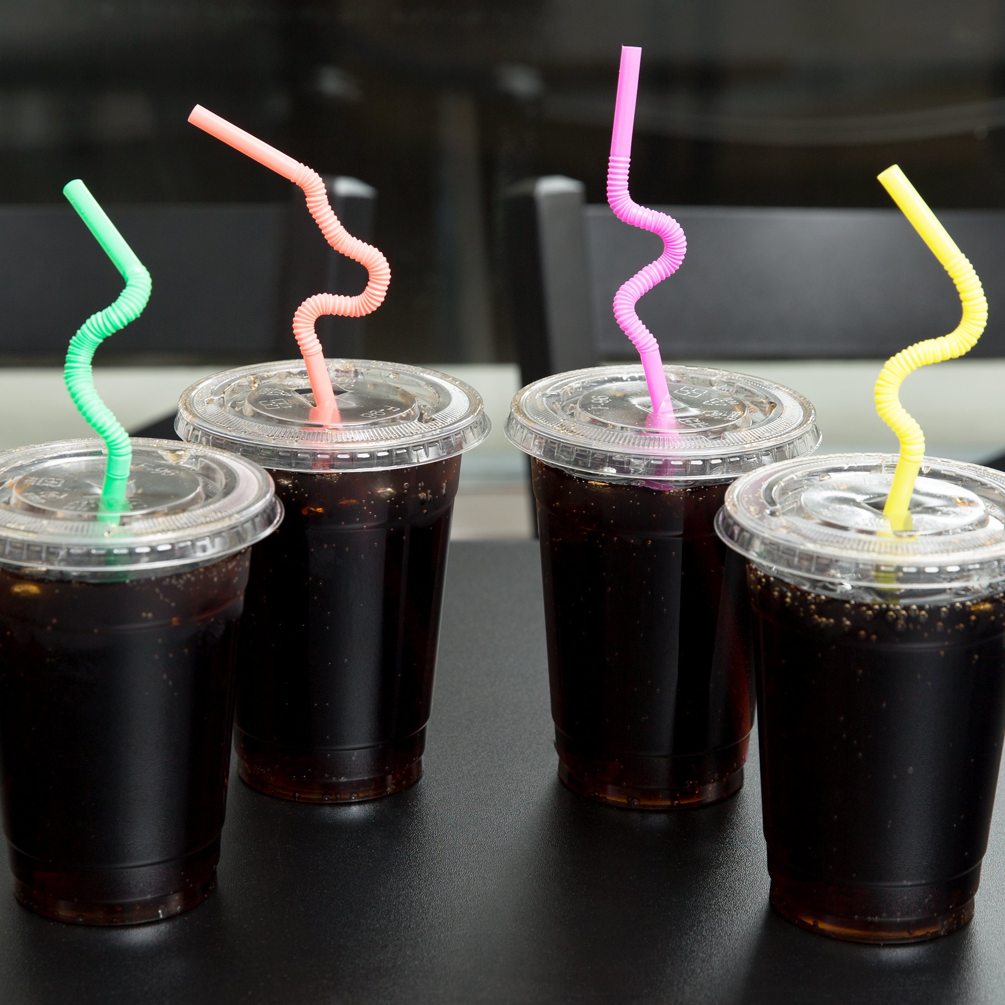 چهار نوشیدنی تیره در فنجان های پلاستیکی شفاف با درب و کاه قابل انعطاف در هر کدام