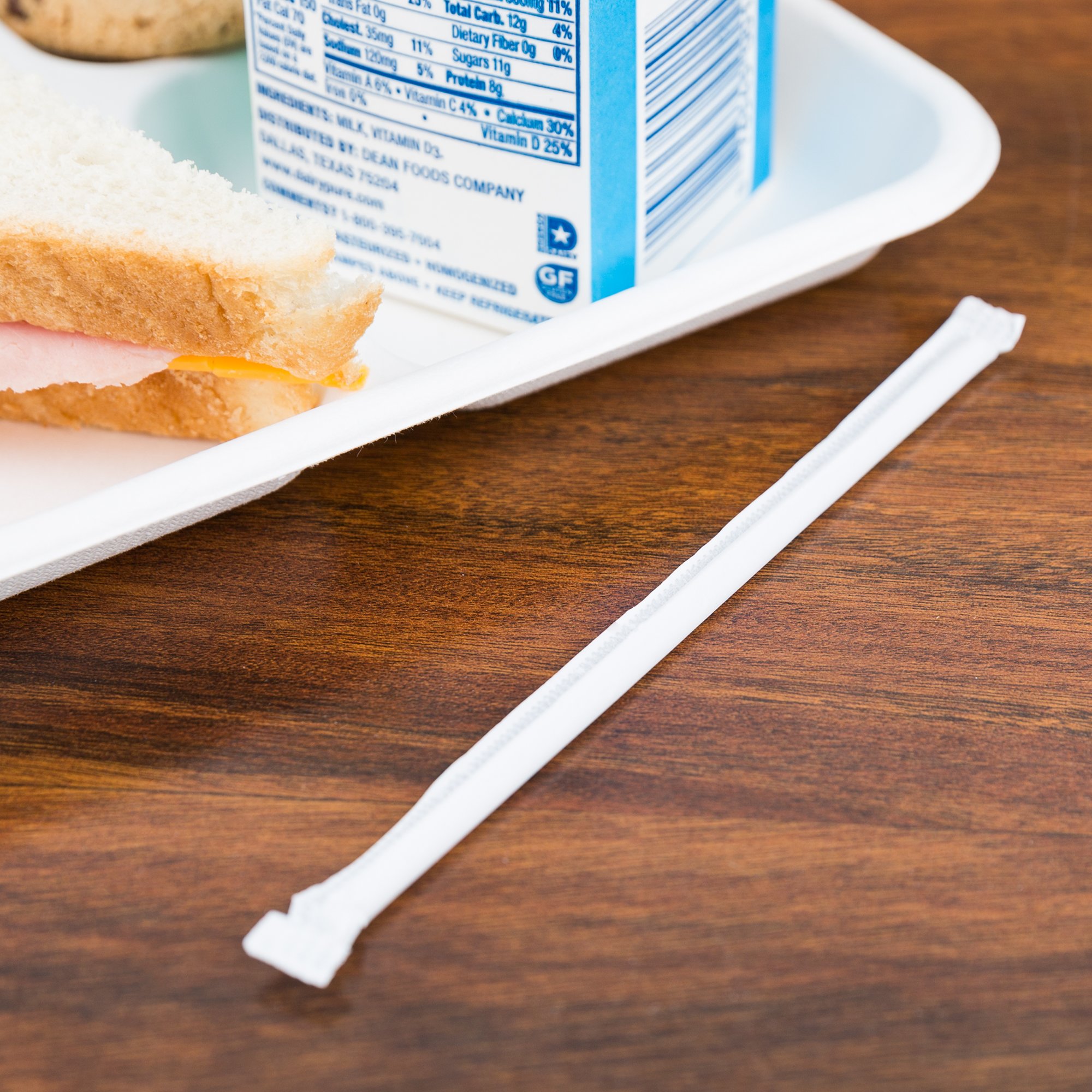 Молочная соломинка в индивидуальной упаковке рядом с обеденным подносом