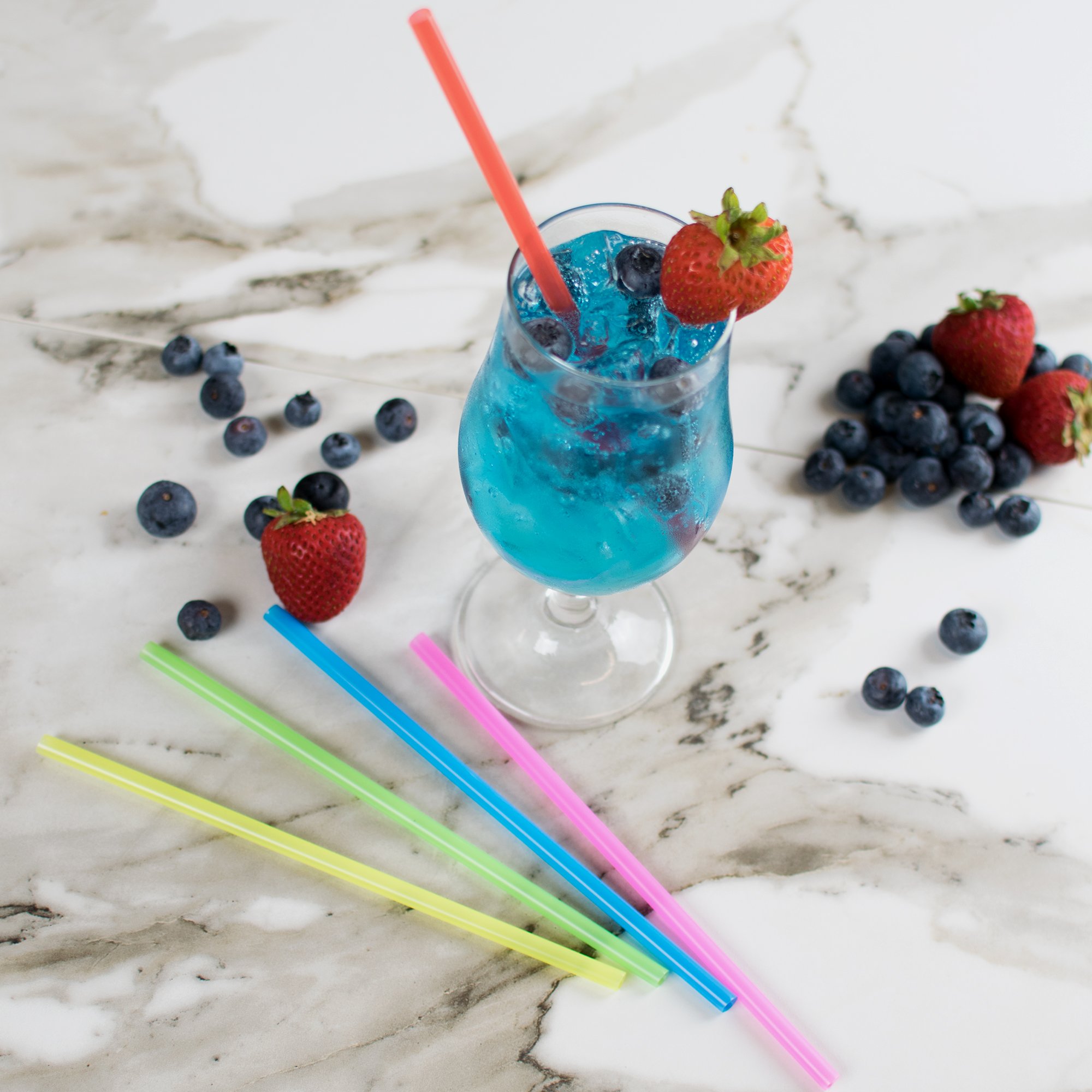 Синий напиток с цветной соломинкой рядом с цветными соломинками, клубникой и черникой