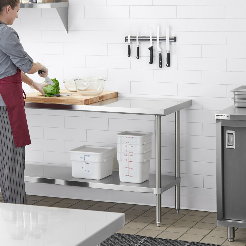 A stainless steel work table with an undershelf, shown in a commercial kitchen setting with storage containers on the lower shelf and a person preparing food on top.