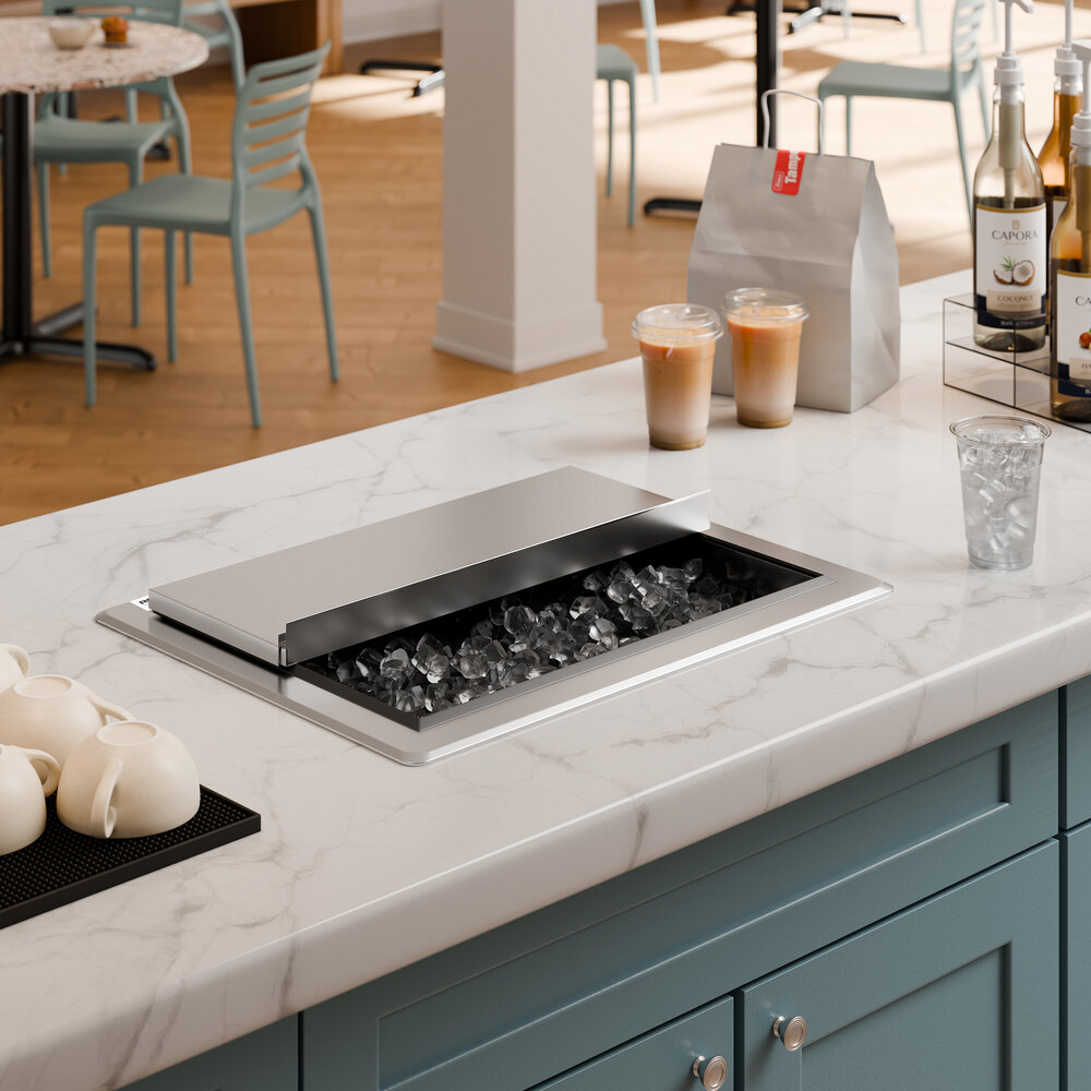 A stainless steel drop-in ice bin with a sliding lid is installed in a marble countertop, partially open to reveal ice inside.