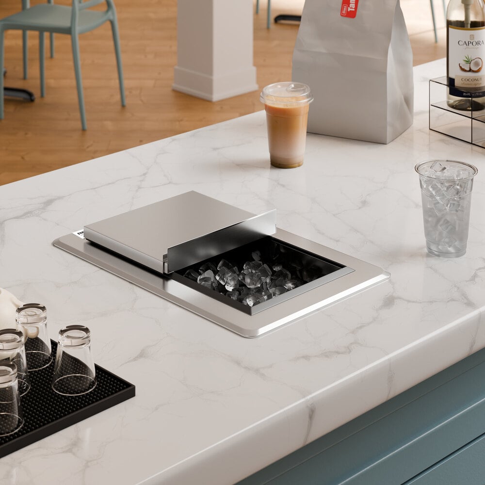 A stainless steel drop-in ice bin with a sliding lid is installed in a marble countertop, partially open to reveal ice inside.