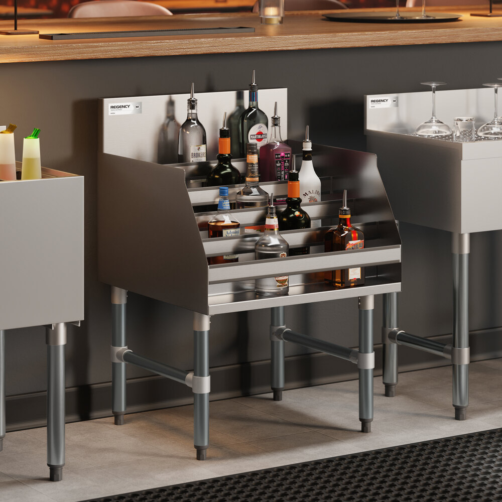 A stainless steel five-tiered liquor display rack filled with various bottles, positioned behind a bar counter.