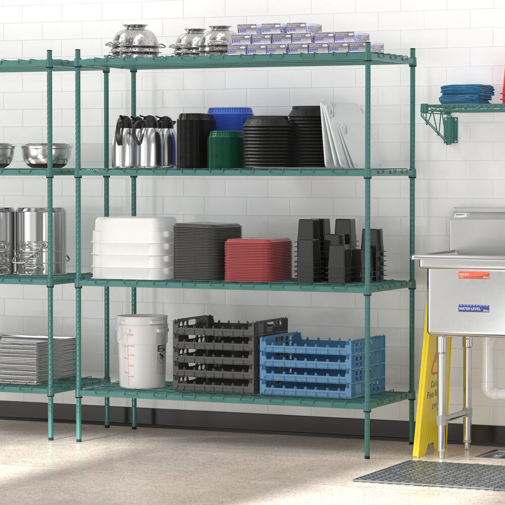 A green metal shelving unit with multiple shelves holding various kitchen items such as bowls, trays, containers, and dish racks, set against a white tiled wall.
