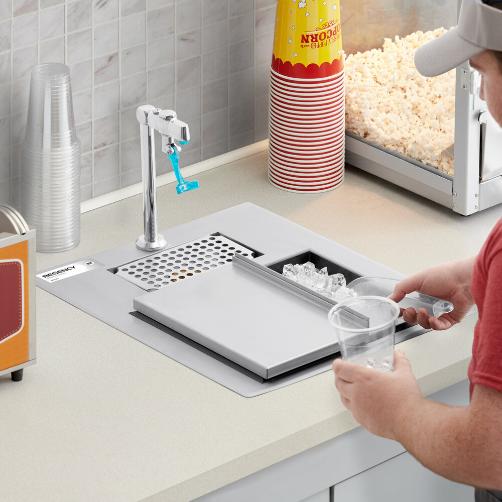 A person is scooping ice from a built-in stainless steel ice bin and water station on a countertop, with popcorn and cups visible nearby.