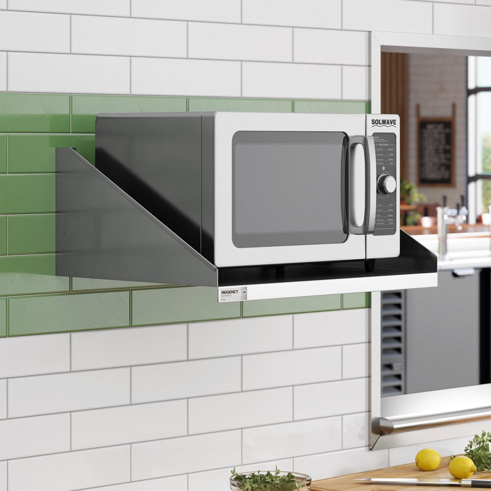 A stainless steel microwave shelf mounted on a tiled kitchen wall, holding a microwave oven.