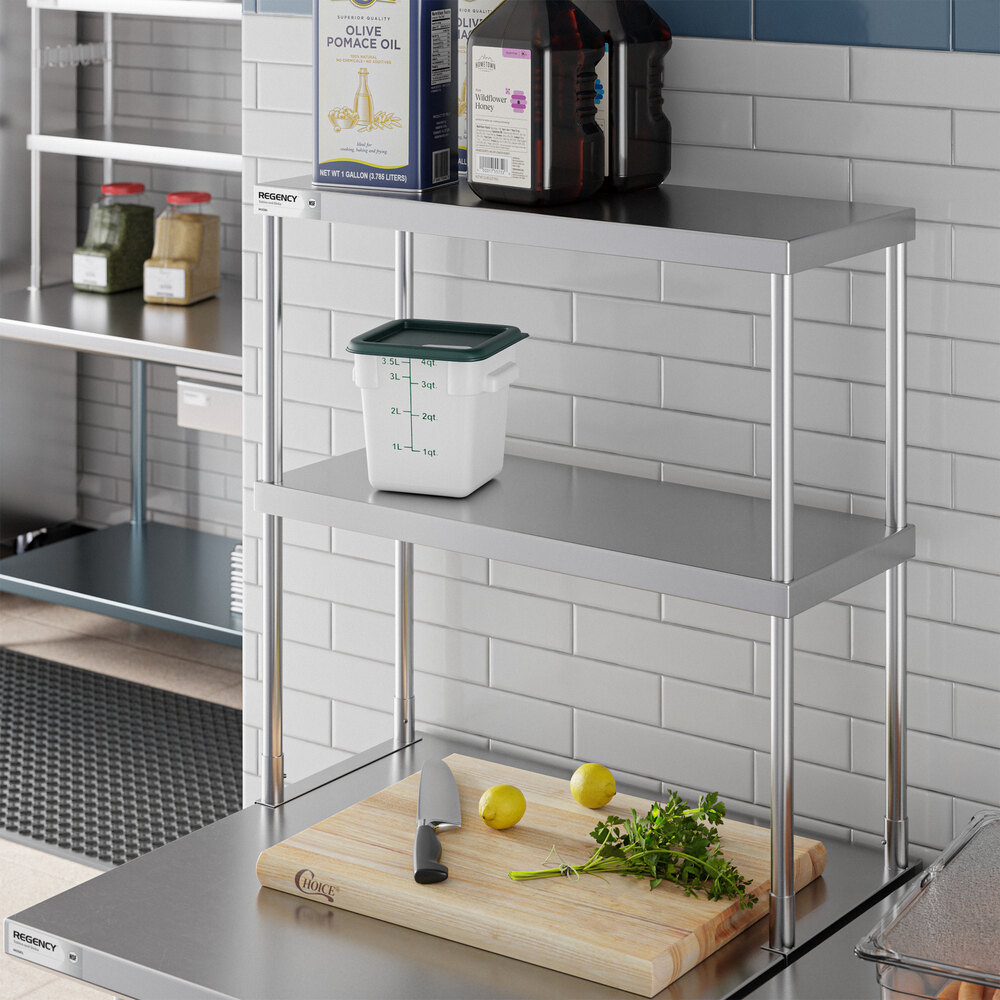 A stainless steel double-deck overshelf with two shelves, placed on a countertop in a kitchen setting, holding containers and kitchen items.