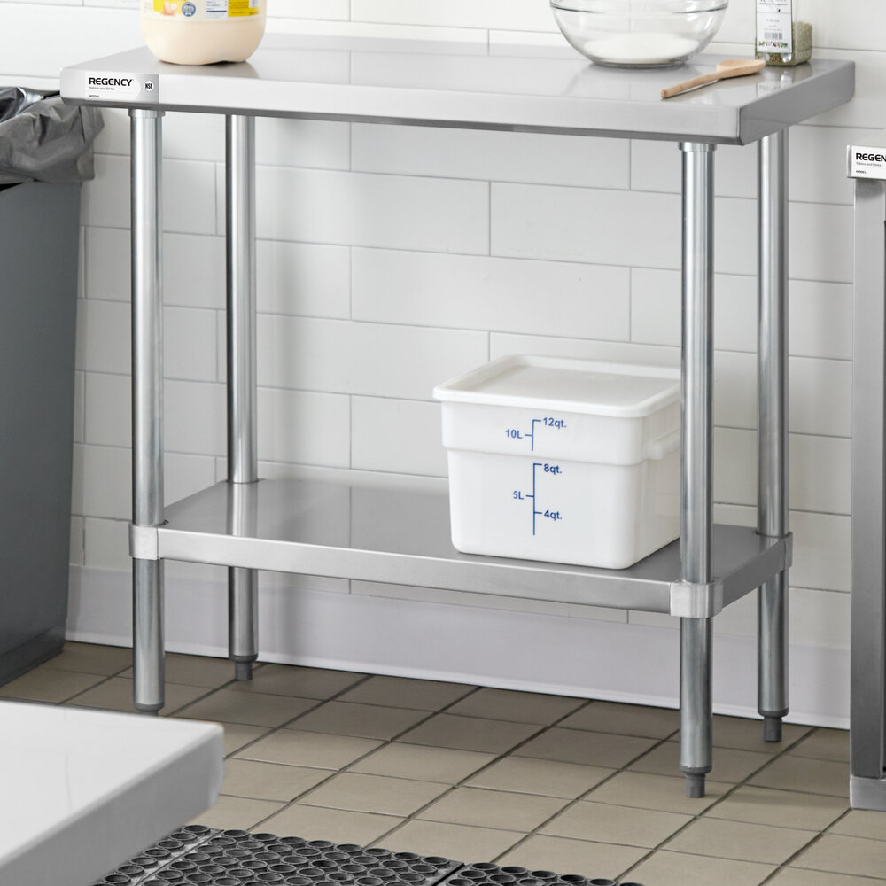 A stainless steel work table with an undershelf, holding a white plastic container with blue measurement markings.