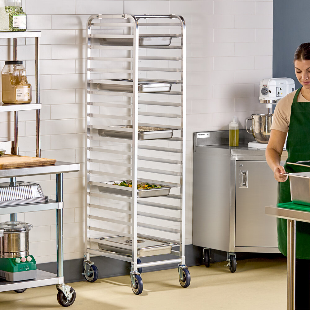 A tall, silver metal rack with multiple horizontal slots holding trays, situated in a commercial kitchen setting.