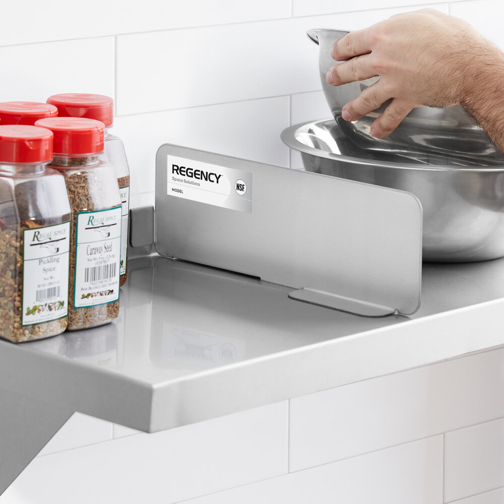 A stainless steel divider is attached to a wall shelf, separating spice containers from metal mixing bowls and a person's hands.