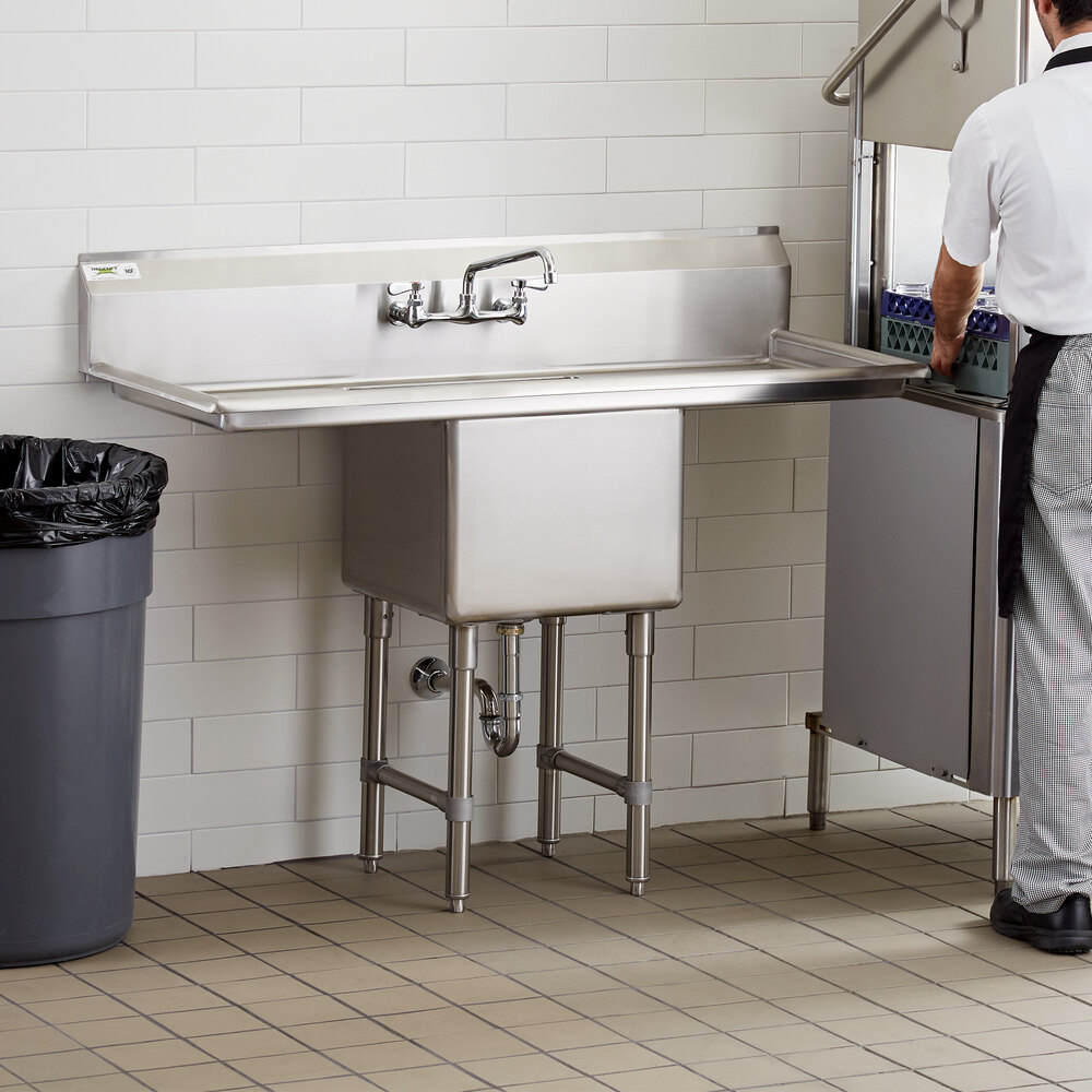 A man standing next to a Regency stainless steel commercial sink with drainboards.