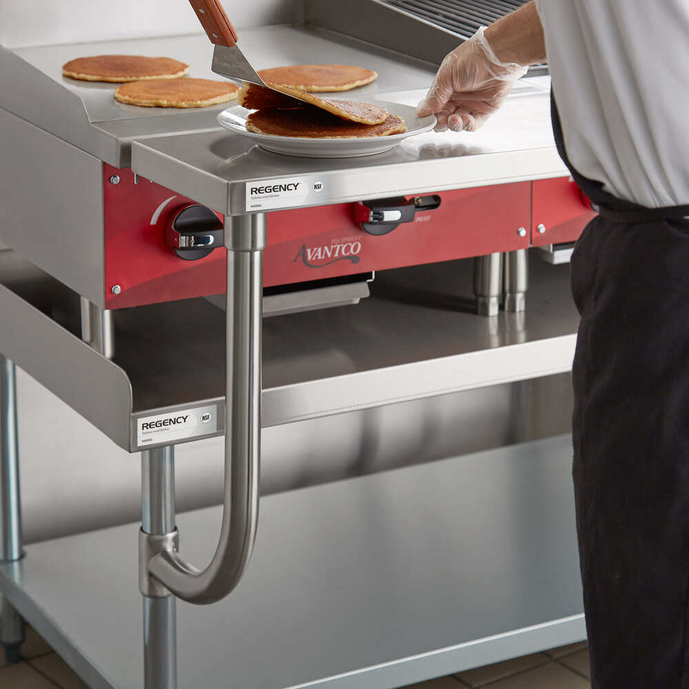 A person is placing pancakes onto a plate on a stainless steel work surface attached to a commercial kitchen equipment stand.