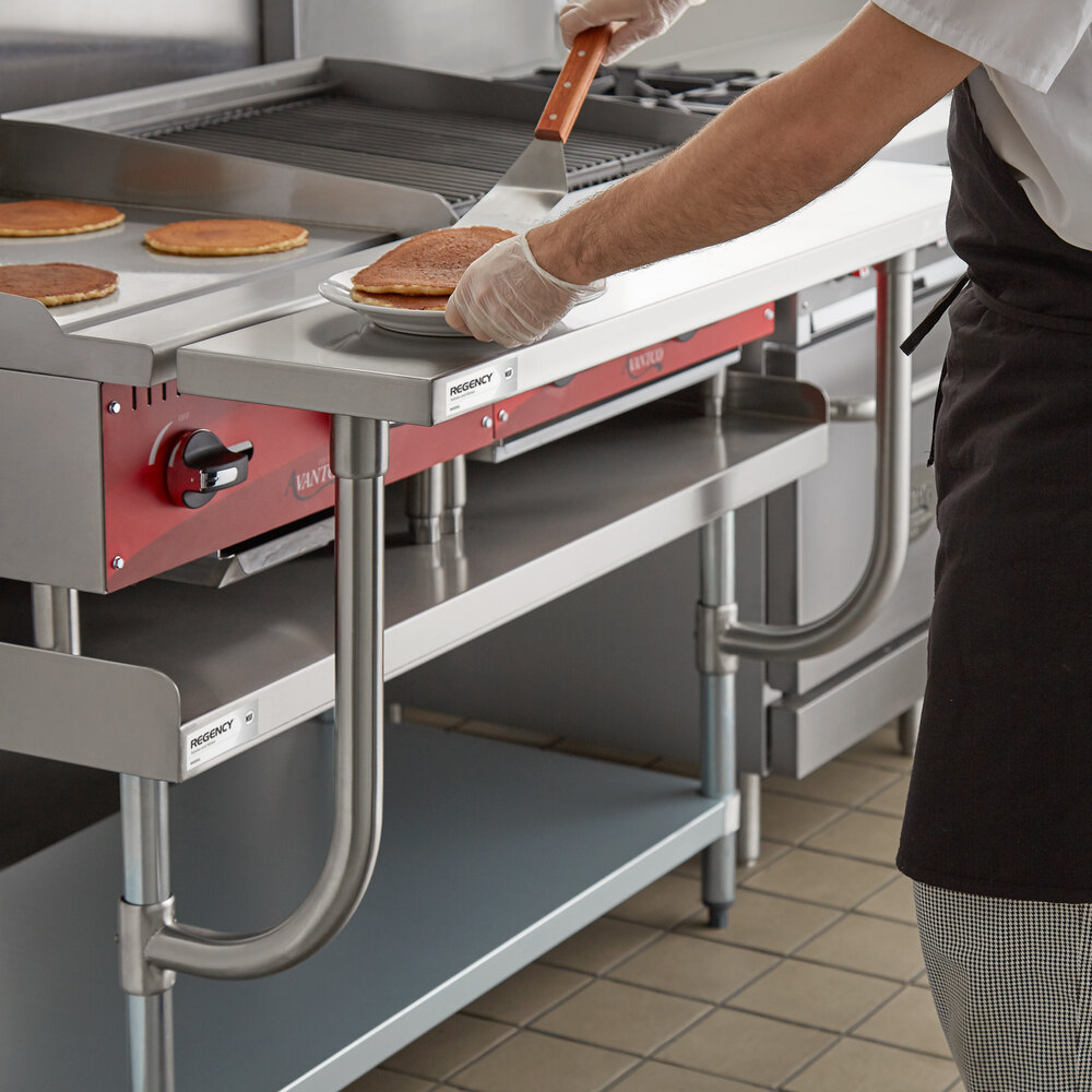 A person is placing pancakes onto a stainless steel work surface attached to a commercial kitchen equipment stand.
