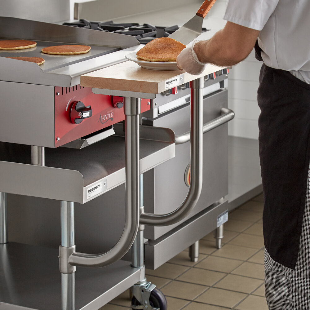 A person is placing pancakes onto a plate on a wooden cutting board attached to a commercial kitchen equipment stand.