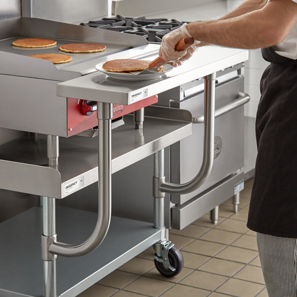 A person is placing a pancake onto a plate on a stainless steel work surface attached to a commercial kitchen equipment stand.