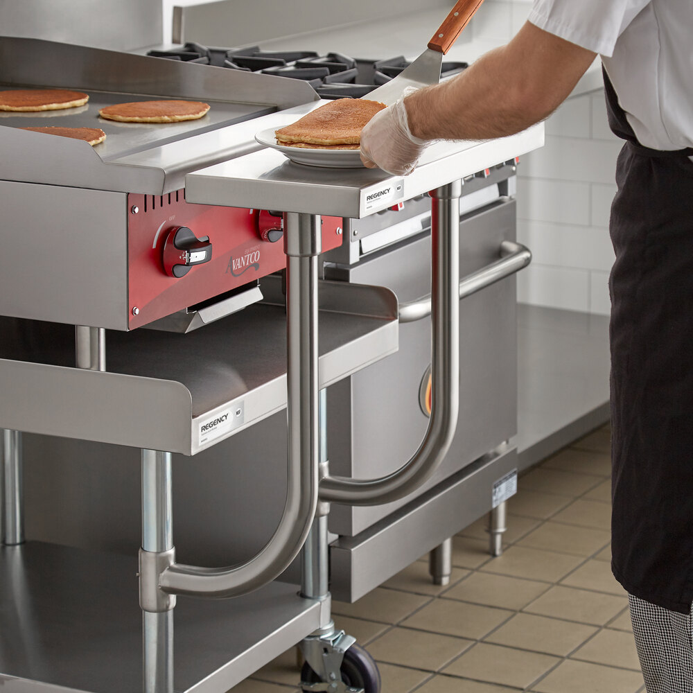 A person is using a stainless steel adjustable work surface attached to a commercial kitchen equipment stand, placing pancakes onto a plate.