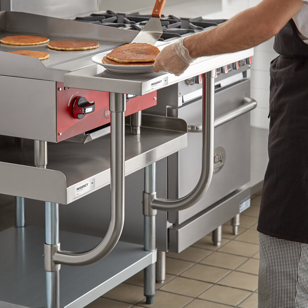 A person is placing pancakes onto a plate on a stainless steel work surface attached to a commercial kitchen equipment stand.