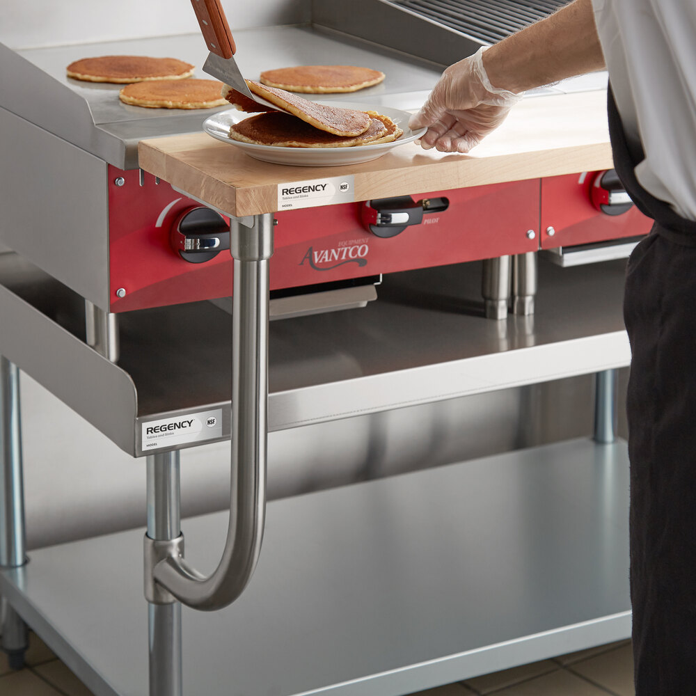 A person is placing pancakes onto a plate on a wooden cutting board attached to a commercial kitchen equipment stand.