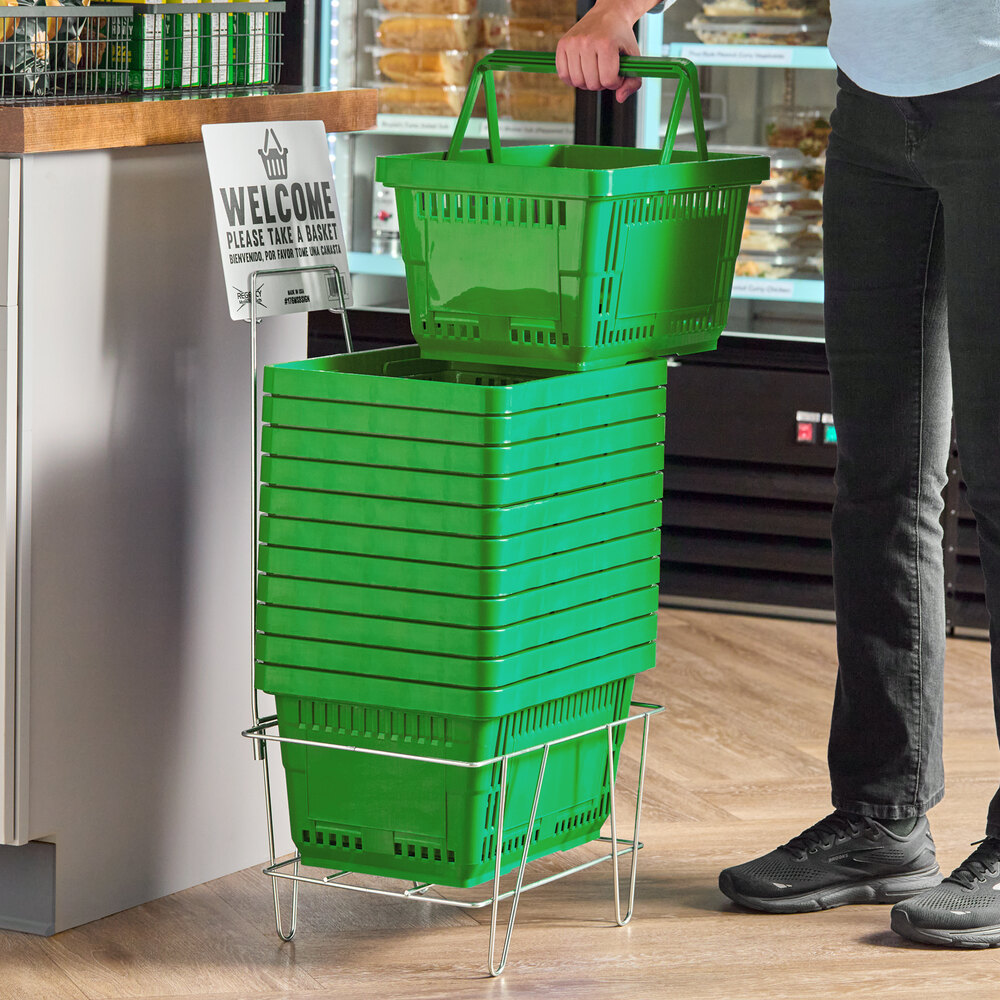 A stack of green plastic grocery market shopping baskets with a metal stand and a sign.