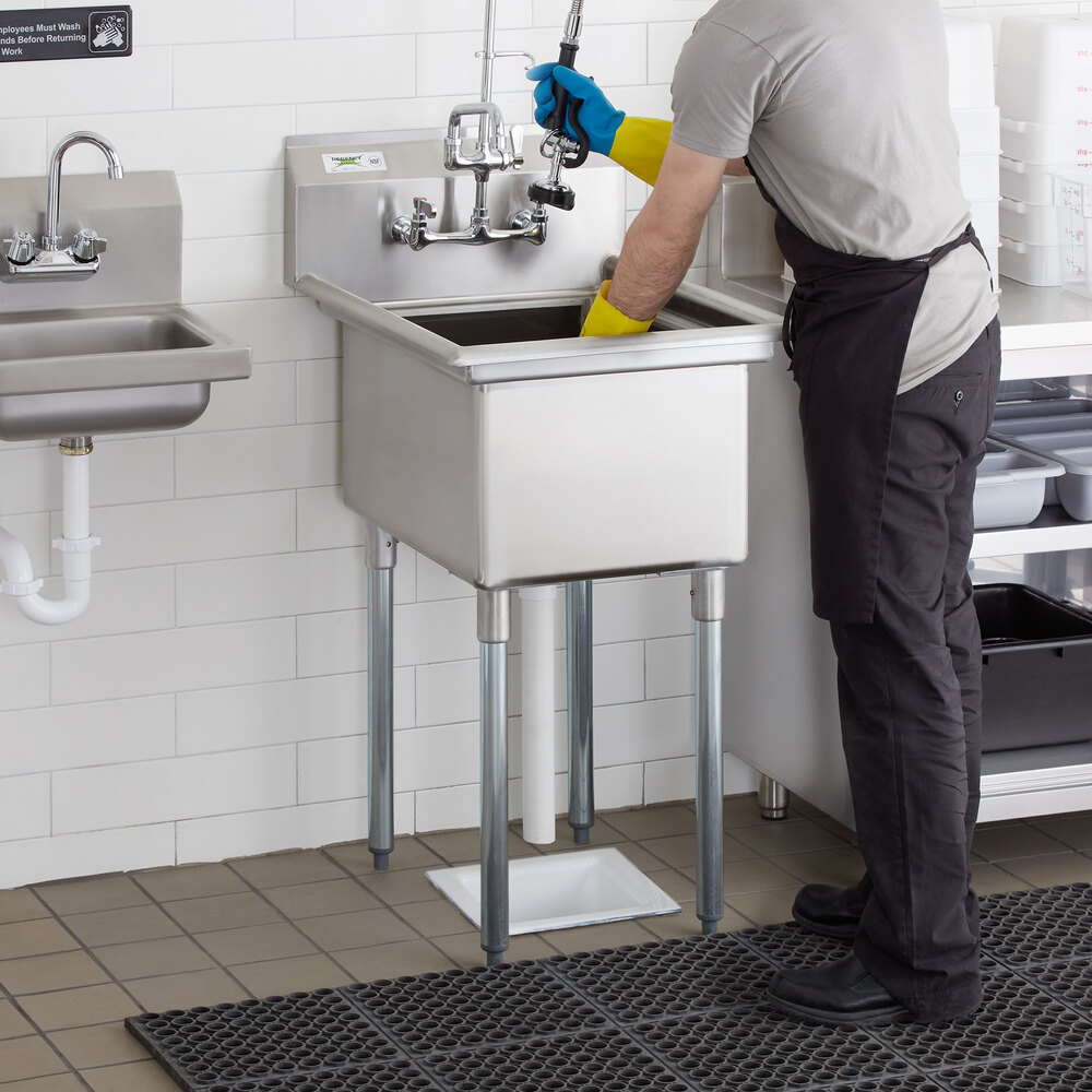 A man in a blue shirt and yellow gloves cleaning a Regency stainless steel sink in a professional kitchen.