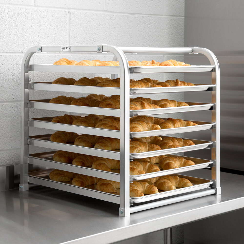 A metal rack holding seven trays filled with croissants, placed on a stainless steel countertop.
