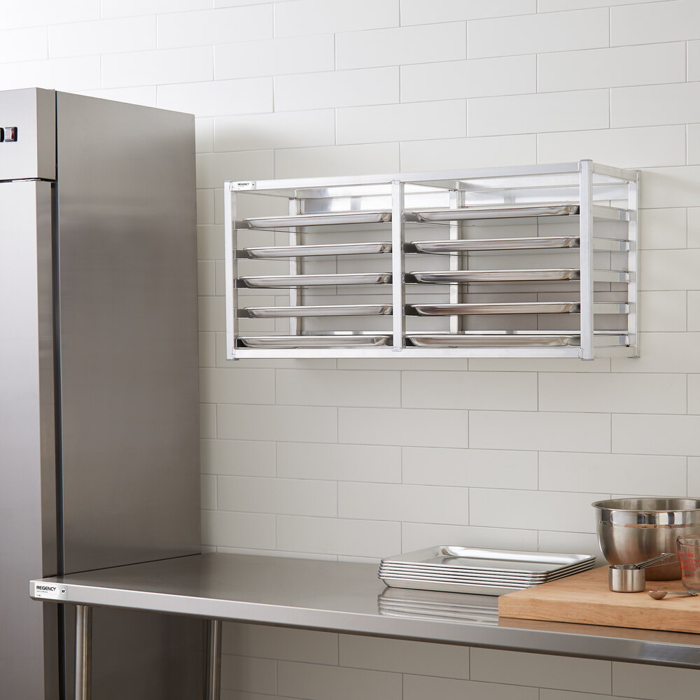 A metal wall-mounted rack holding several sheet pans in a commercial kitchen setting.